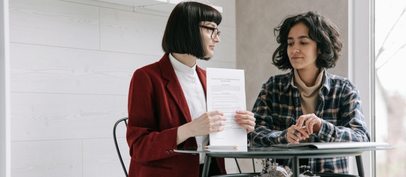 Two women reviewing real estate documents indoors, symbolizing a sale.